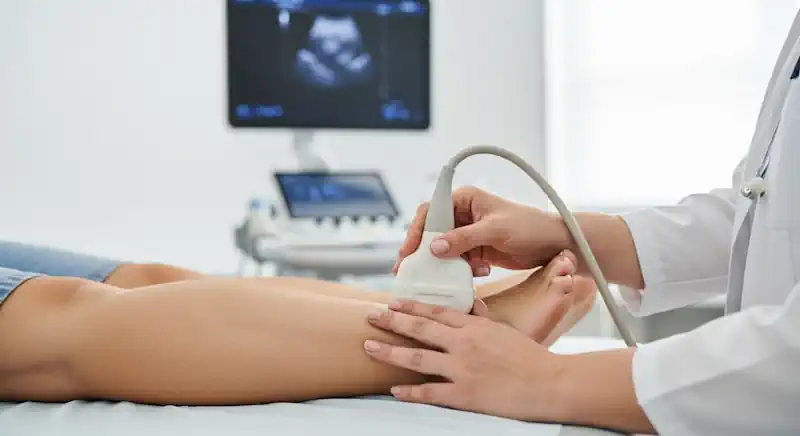 A doctor performing a leg ultrasound on a patient to check for deep vein thrombosis.